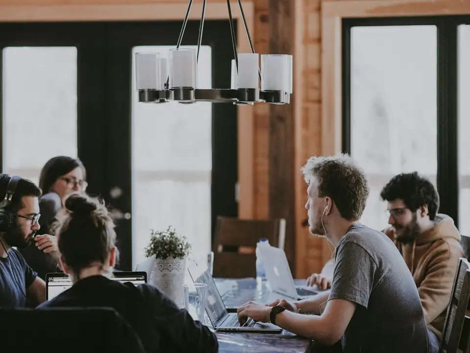Equipo trabajando alrededor de una mesa larga con portátiles